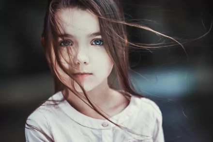 HD desktop wallpaper featuring a close-up portrait of a brunette little girl with striking blue eyes and wind-blown hair, captured in detailed child photography.