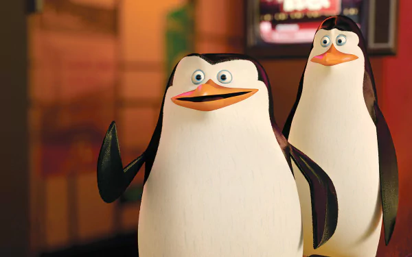 HD PC desktop wallpaper from the movie Penguins of Madagascar showing two animated penguins posing against a warm, softly lit indoor background.