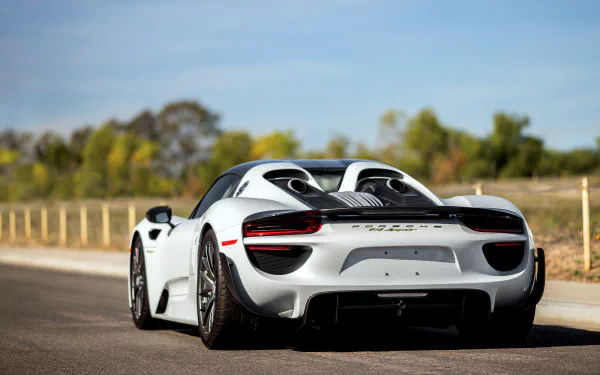 A sleek white Porsche 918 Spyder supercar stands on a sunlit road, showcasing its stunning design and performance. A captivating 4K Ultra HD desktop wallpaper.