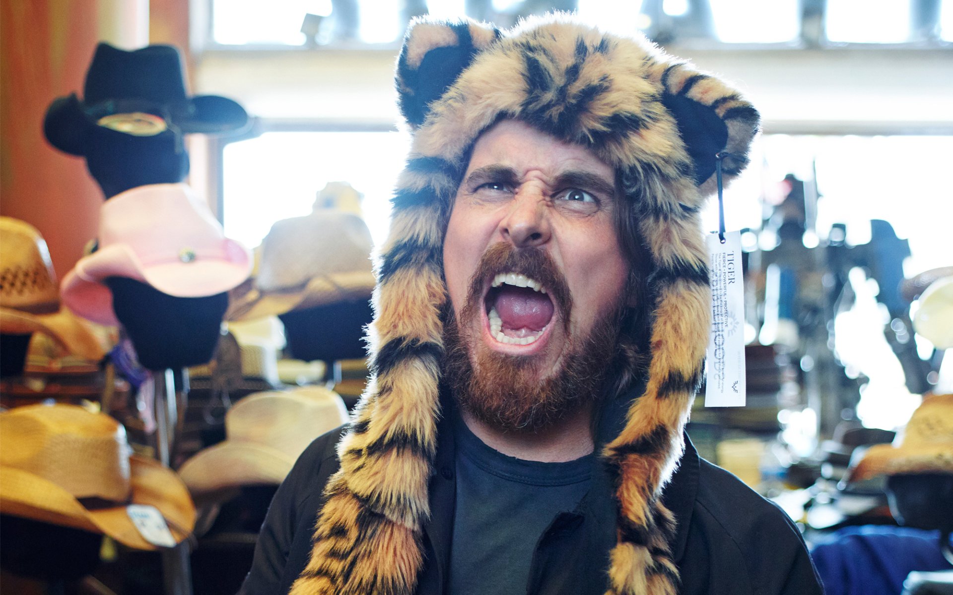 HD PC desktop wallpaper featuring a bearded man wearing a tiger-striped hat, surrounded by various hats in the background, tagged with English actor and celebrity Christian Bale.