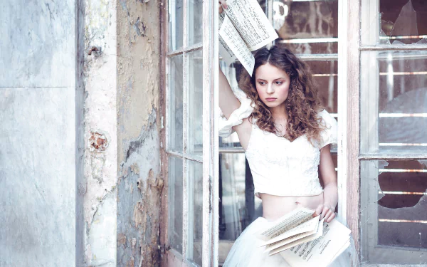 HD PC desktop wallpaper of a brunette woman model with brown eyes in a white dress, holding sheet music and surrounded by pages near a weathered window frame.