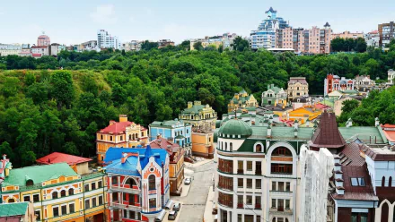 HD PC wallpaper: colorful historic houses and modern buildings on a hillside beside a dense forest in Kyiv, Ukraine, showcasing city and man-made architecture.