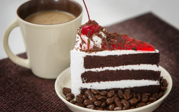 A slice of chocolate cake topped with cherry and whipped cream, surrounded by coffee beans, next to a steaming cup of coffee on a textured surface.