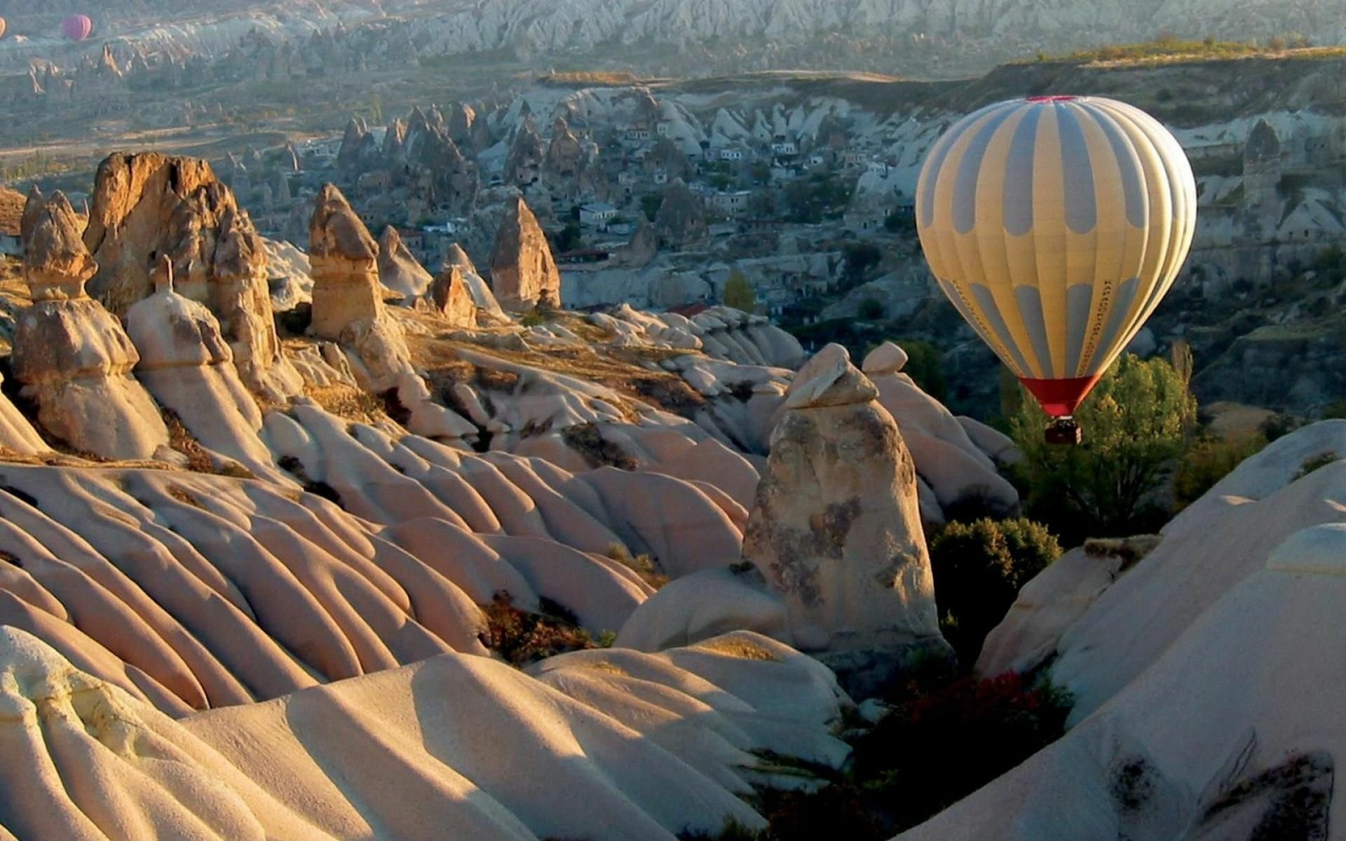 HD desktop wallpaper showing a hot air balloon flying over the rocky landscape of Cappadocia with unique rock formations and valleys.