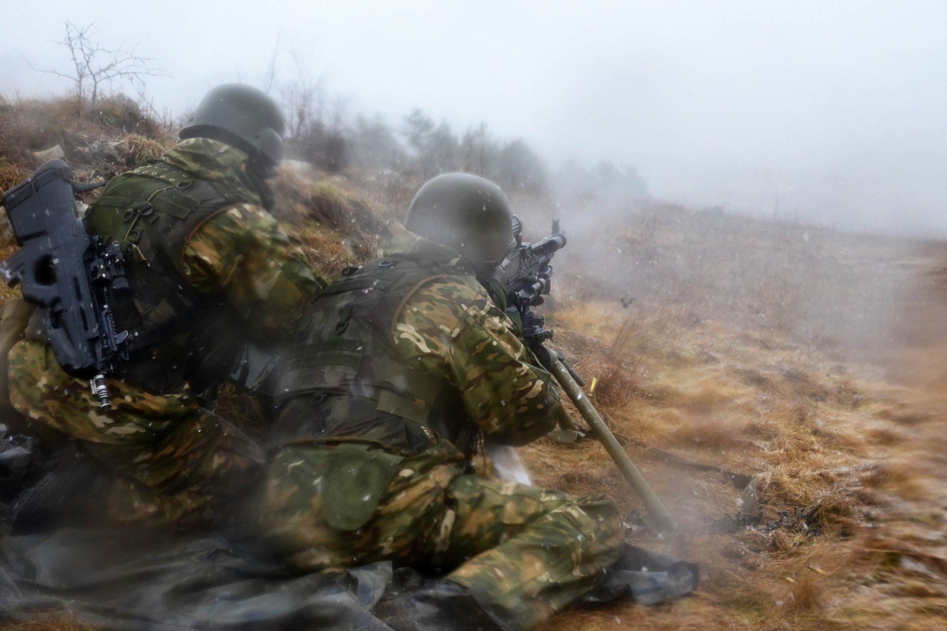 Two soldiers in camouflage gear operate a machine gun in a foggy, rugged terrain, captured in an HD military-themed desktop wallpaper.