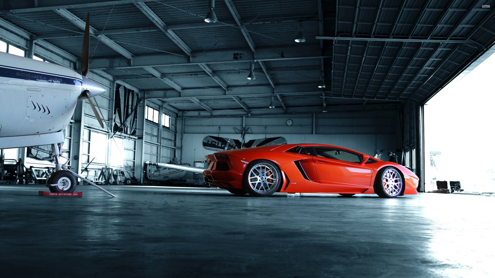 Red Lamborghini Aventador LP 700-4 parked in a hangar beside a private plane — 4K Ultra HD PC desktop wallpaper featuring a sleek vehicle.