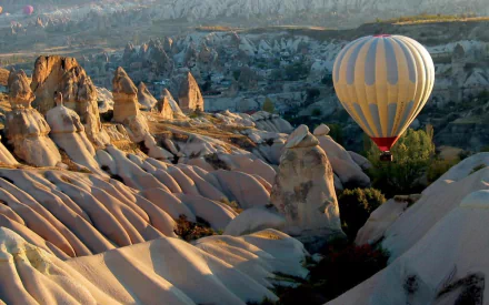 HD desktop wallpaper showing a hot air balloon flying over the rocky landscape of Cappadocia with unique rock formations and valleys.