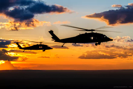 Silhouettes of two Sikorsky UH-60 Black Hawk attack helicopters flying against a vibrant sunset sky with scattered clouds, captured in HD desktop wallpaper quality.