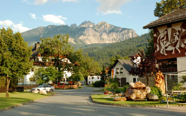 A charming Austrian street with traditional houses, greenery, and mountains in the background, showcasing man-made architecture in an HD desktop wallpaper setting.