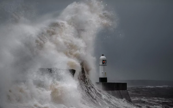 A powerful ocean wave crests and crashes against a man-made lighthouse during a storm, captured in HD for a striking desktop wallpaper background.