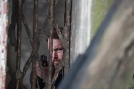 Close-up of a bearded man aiming a pistol through rusted beams in a tense scene from the movie Criminal (2016). 4K Ultra HD PC wallpaper.