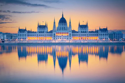 The Hungarian Parliament Building in Budapest showcases its iconic dome and spires, reflected calmly in the water at sunrise, highlighting intricate architecture and monument grandeur.