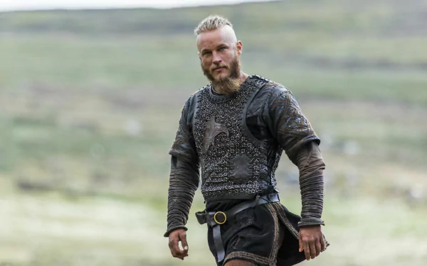 Ragnar Lothbrok, portrayed by Travis Fimmel in the TV show Vikings (2013), stands confidently in a detailed armored costume, set against a vast, natural backdrop.