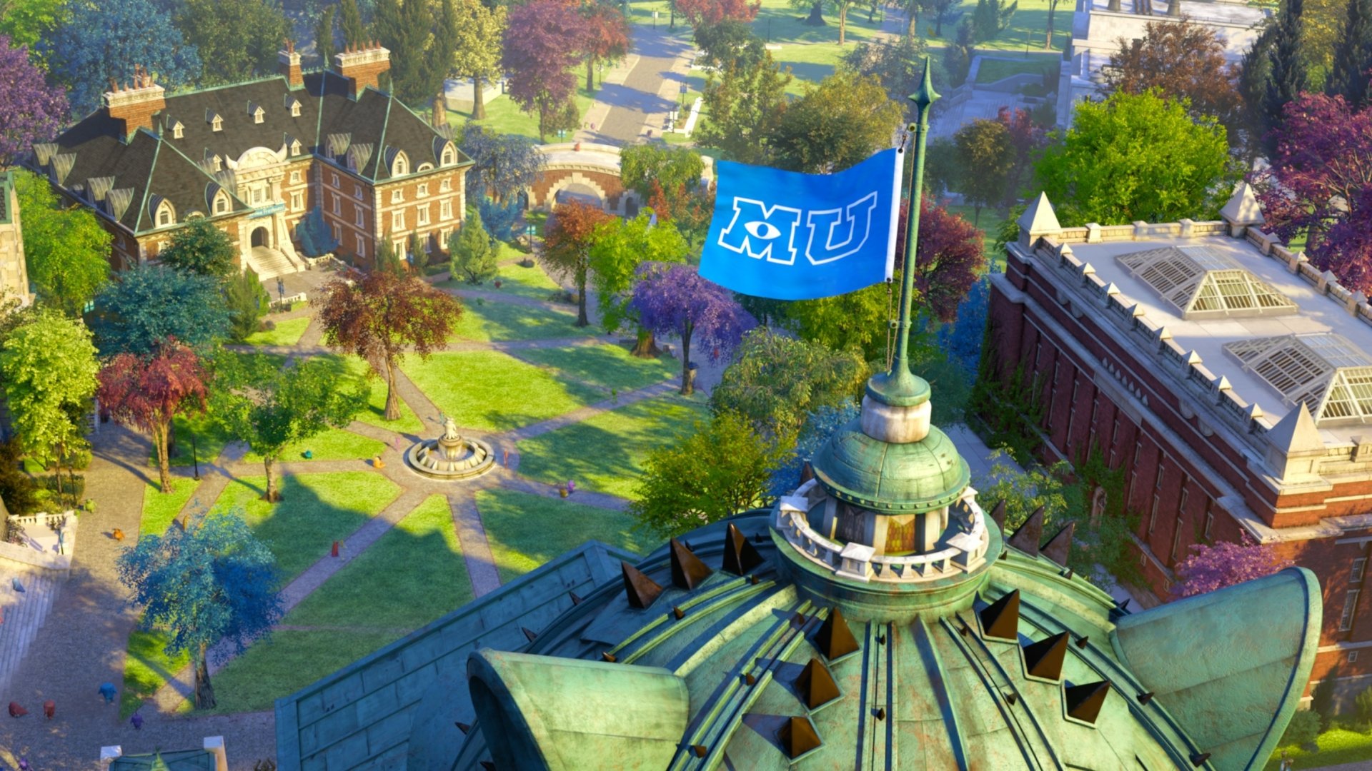 Aerial view of Monsters University campus with MU flag above a domed building, colorful quad and surrounding academic halls — 2K Quad HD PC desktop wallpaper.