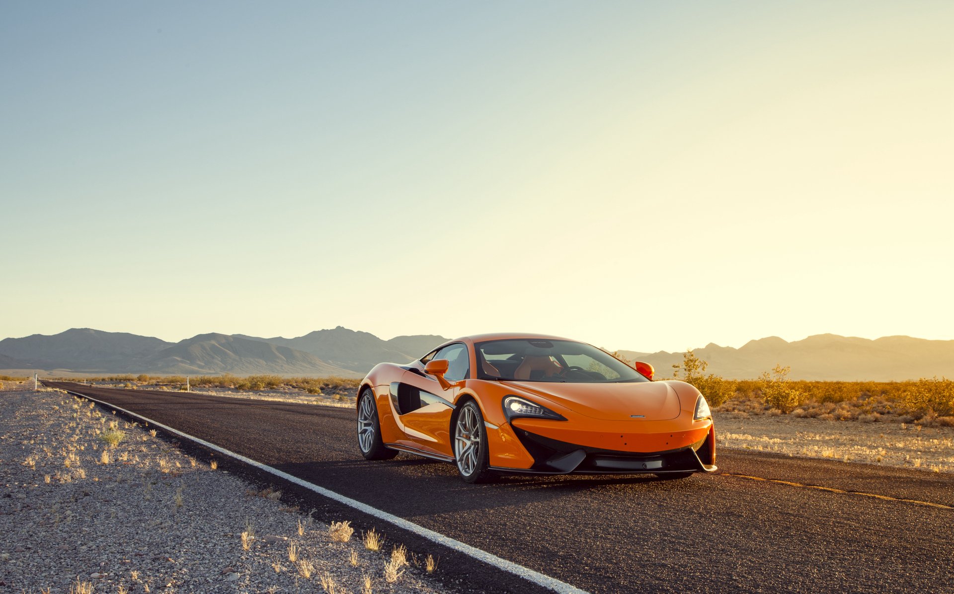 Orange McLaren 570S sports car parked on a deserted road at sunset, captured in a 4K Ultra HD desktop wallpaper.