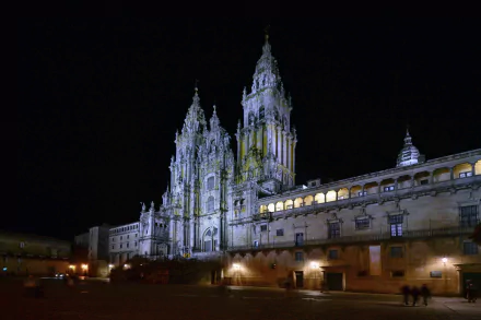Night view of the illuminated Santiago de Compostela Cathedral in Spain, showcasing its intricate religious architecture in a vibrant city square.