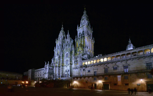 Night view of the illuminated Santiago de Compostela Cathedral in Spain, showcasing its intricate religious architecture in a vibrant city square.