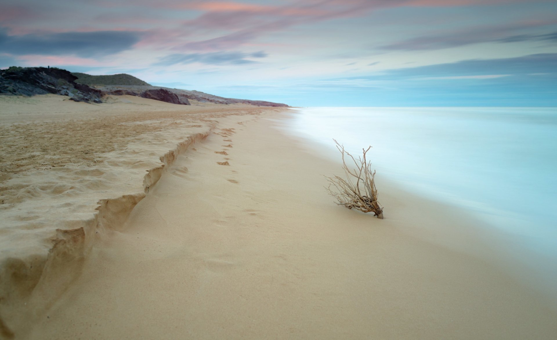 HD PC desktop wallpaper: tranquil sandy beach coastline meeting the horizon under a pastel sky, smooth surf and a lone driftwood nature background.
