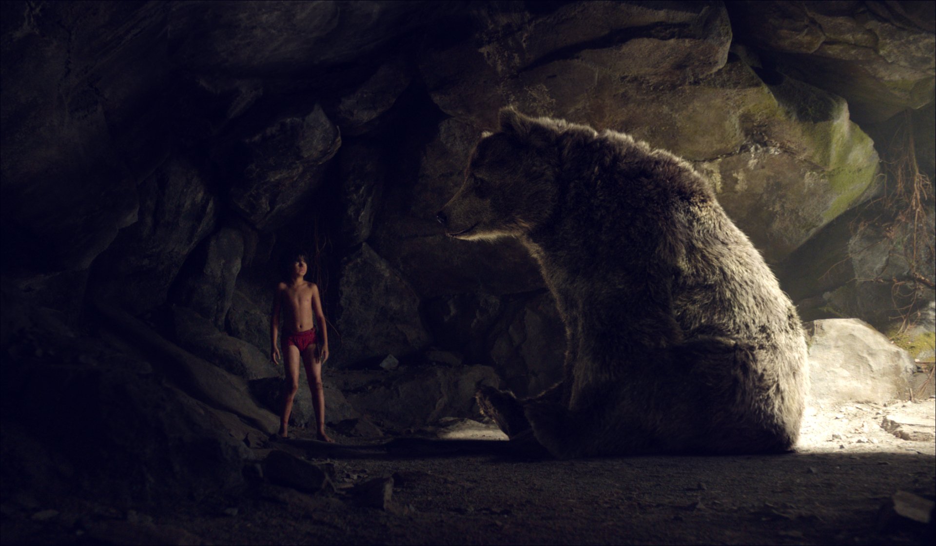 HD PC desktop wallpaper from the movie The Jungle Book (2016) showing Mowgli standing inside a dark cave facing a large bear.