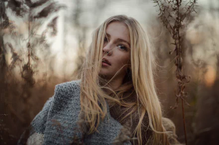 8K Ultra HD desktop wallpaper: close bokeh portrait of a blonde woman model with blue eyes wearing a cozy scarf, soft natural light and warm autumn tones.
