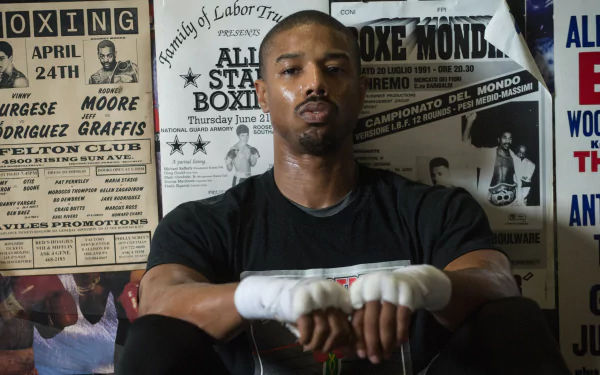 4K Ultra HD PC desktop wallpaper of Adonis Creed from the movie Creed — a boxer with wrapped hands seated against gym posters, focused and contemplative.