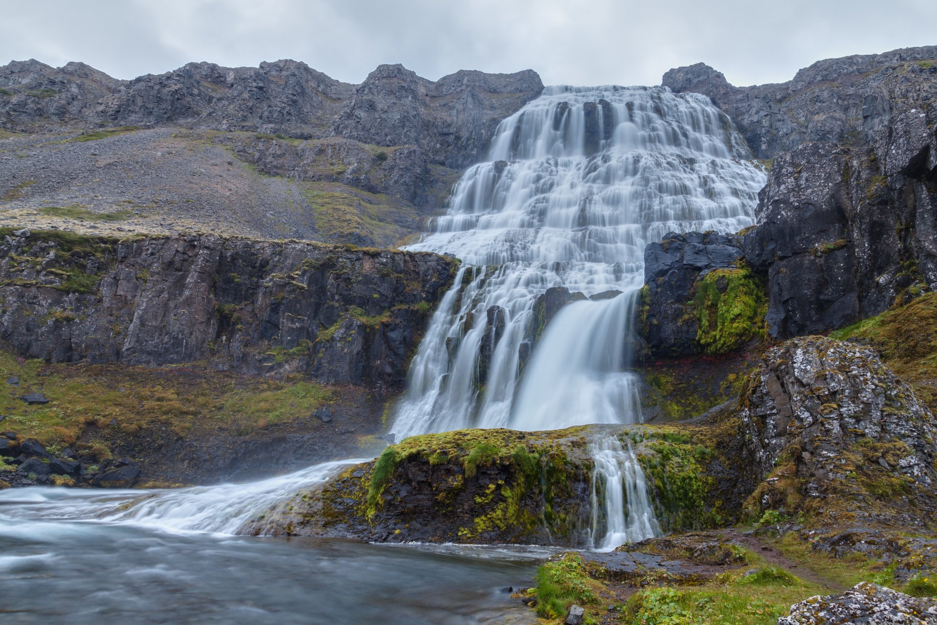 Dynjandi waterfall in Iceland cascading over tiered cliffs with mossy rocks and a calm pool, 5K Ultra HD PC desktop wallpaper and background.