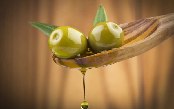 Close-up of two green olives with leaves on a wooden spoon dripping golden olive oil, captured in 4K Ultra HD for a rich, detailed food background.
