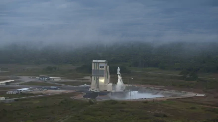 HD PC desktop wallpaper of a man-made spaceport: rocket launching from a wet launch pad beside a service tower, mist and low clouds over surrounding fields.