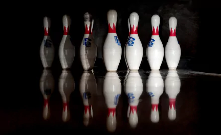 A close-up of bowling pins with striking red accents, reflected on a smooth surface, highlighting the sport's dynamic essence in this HD desktop wallpaper.