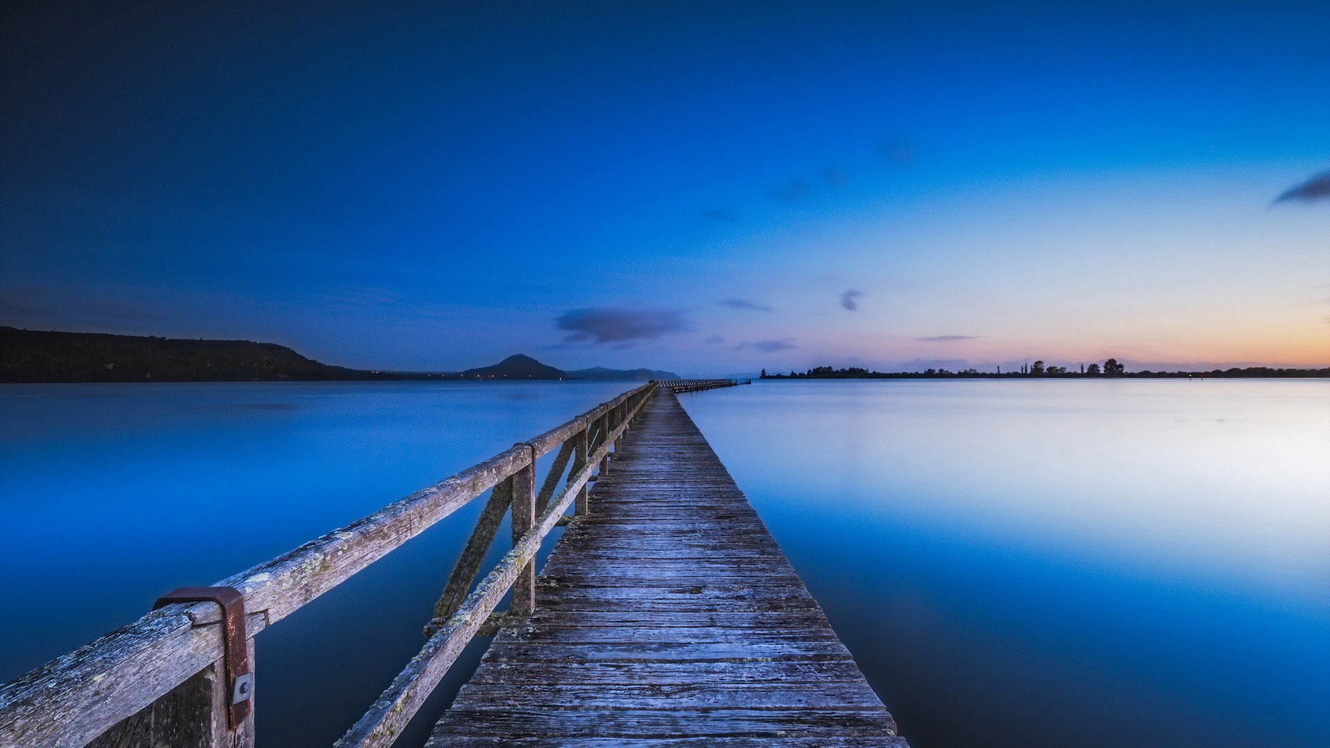 HD PC desktop wallpaper of a blue ocean at dusk, a man-made wooden pier stretching into the calm horizon as the sky fades from deep blue to twilight.