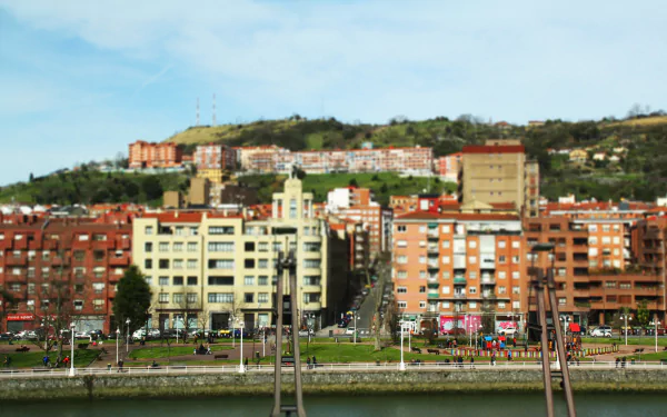 4K Ultra HD PC desktop wallpaper: Bilbao riverfront in Spain — man-made embankment with multi-story city buildings beneath a green hillside.