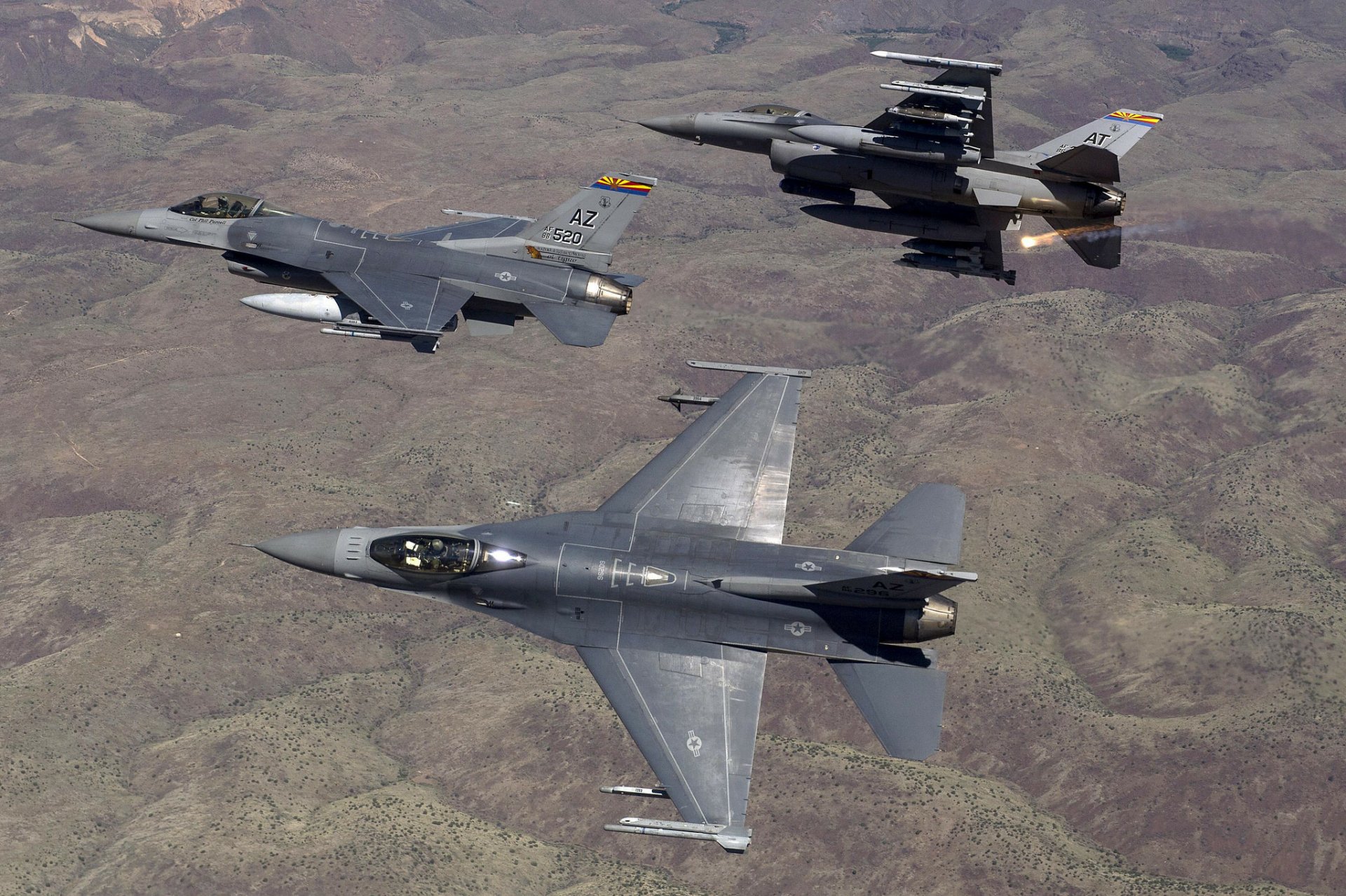 Three General Dynamics F-16 Fighting Falcon jet fighters in formation over arid terrain, military warplane aircraft; HD PC desktop wallpaper/background.