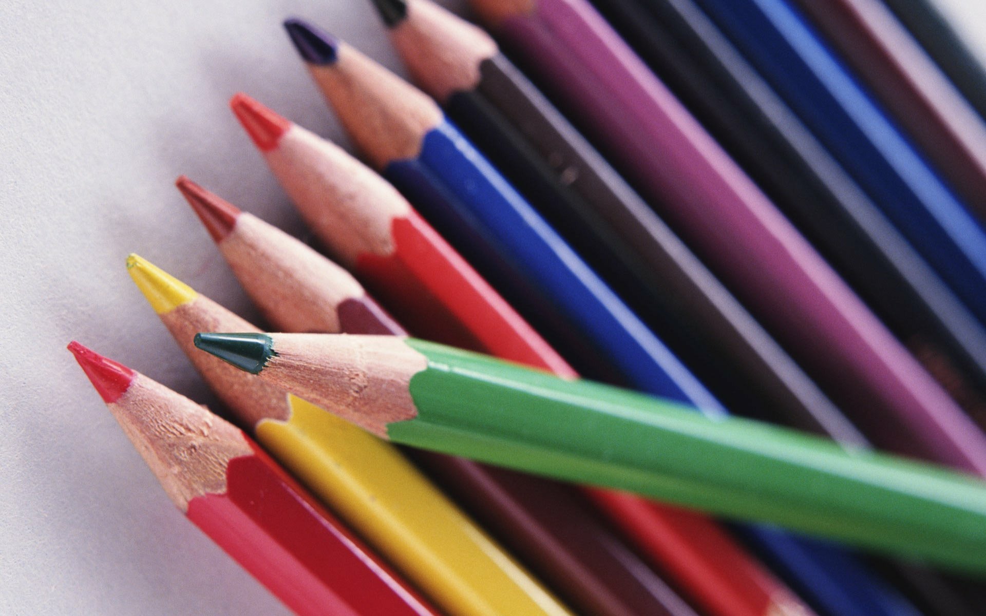 HD PC desktop wallpaper photo of sharpened colored pencils fanned diagonally, vivid reds, greens, blues on a soft white background.