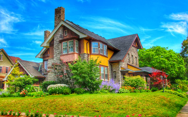 A vibrant garden surrounds a charming house in Ontario, Canada, showcasing a beautiful blend of colorful flowers and lush greenery against a bright blue sky.