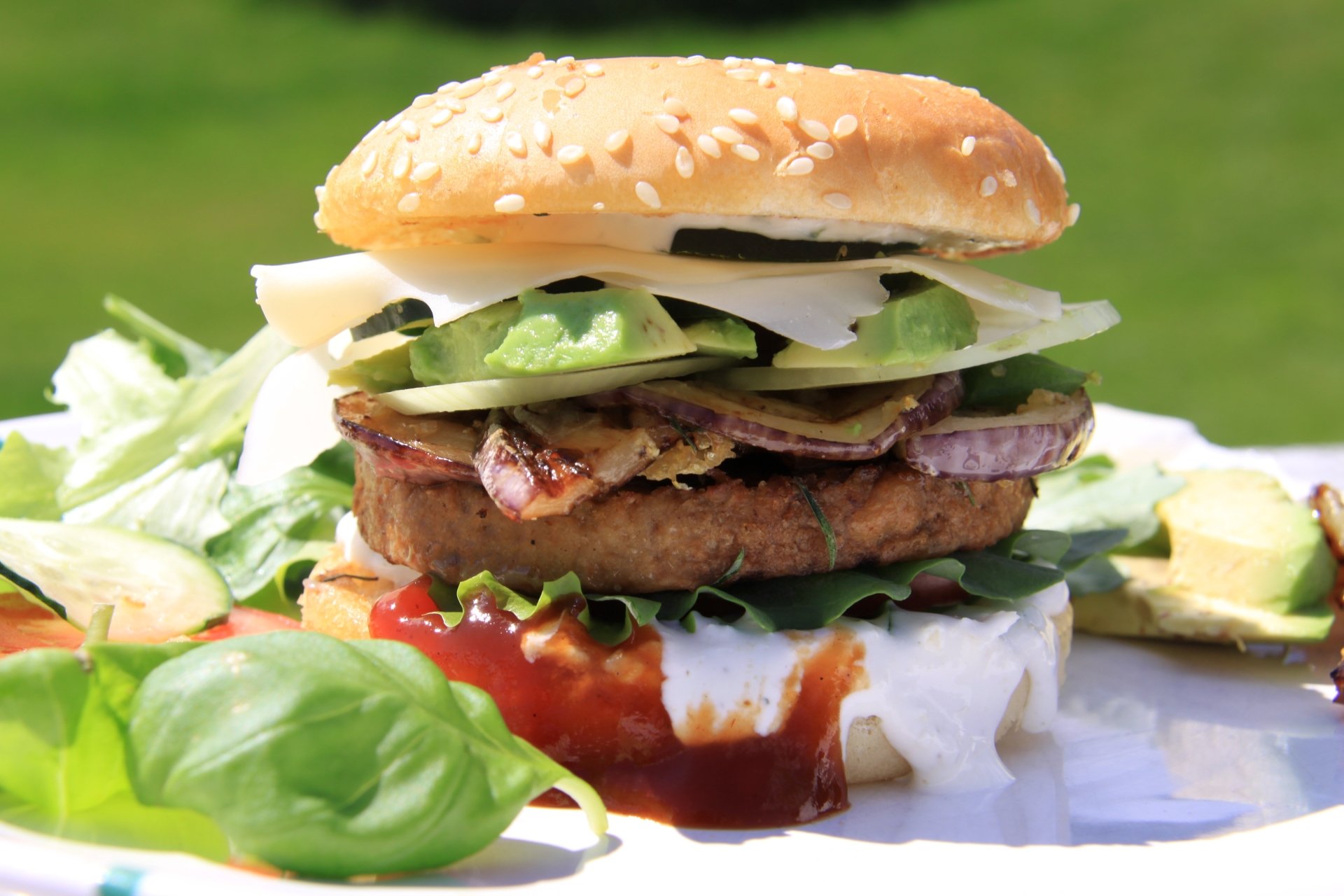 A close-up 4K Ultra HD image of a hamburger with lettuce, onions, avocado, and sauce, served alongside a fresh salad on a bright green background.