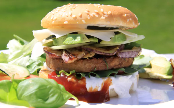 A close-up 4K Ultra HD image of a hamburger with lettuce, onions, avocado, and sauce, served alongside a fresh salad on a bright green background.