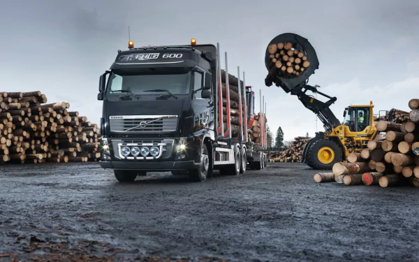 HD desktop wallpaper featuring a Volvo truck loaded with logs at a logging site, alongside heavy machinery handling timber.