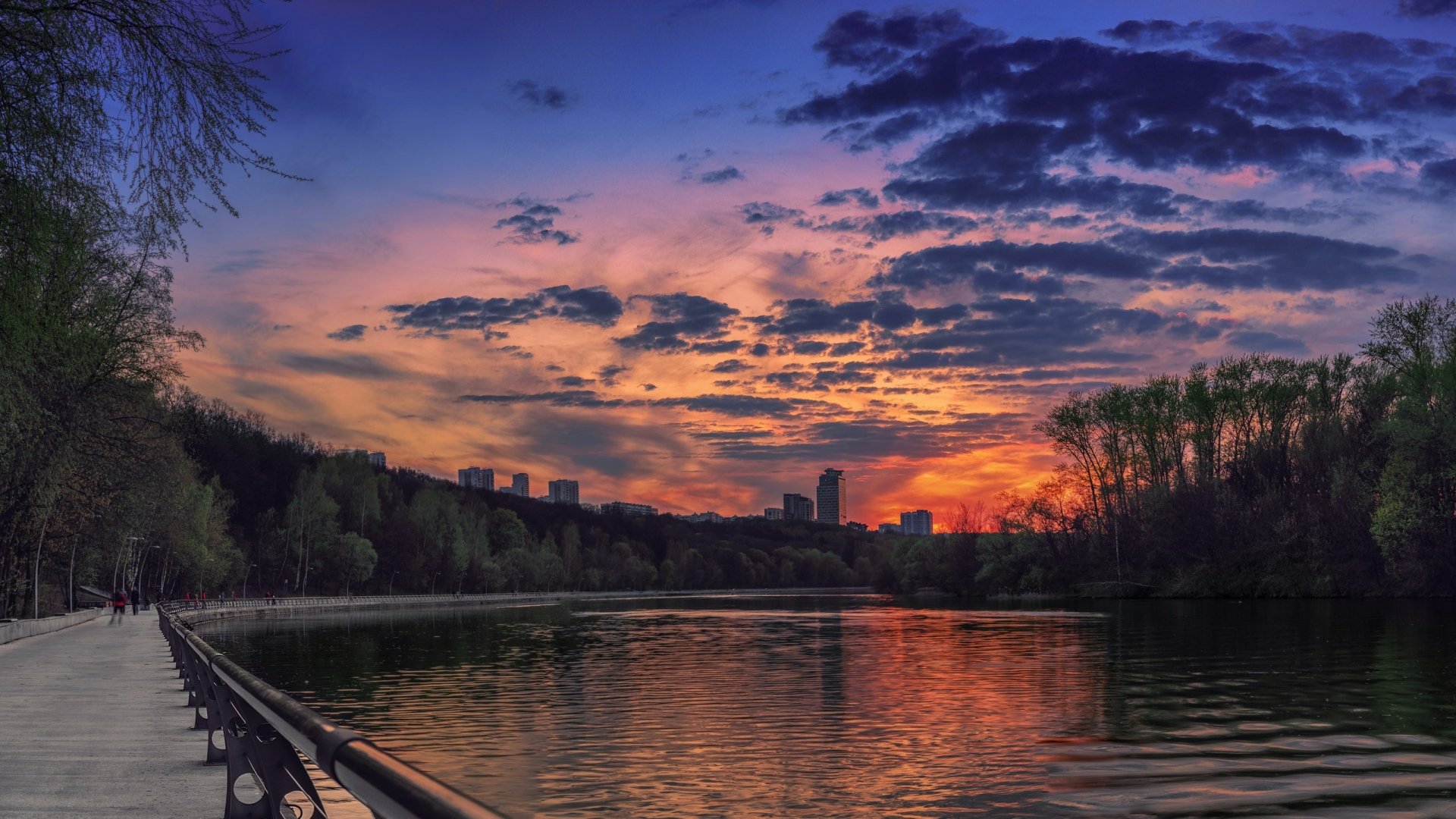 HD photography of a vibrant sunset over a calm river, with silhouetted trees and city skyline, captured as a stunning PC desktop wallpaper and background.