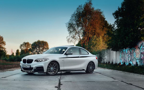 White BMW coupe parked on cracked concrete beside a graffiti wall at dusk — 5K Ultra HD PC desktop wallpaper and background showcasing a vehicle in an urban setting.