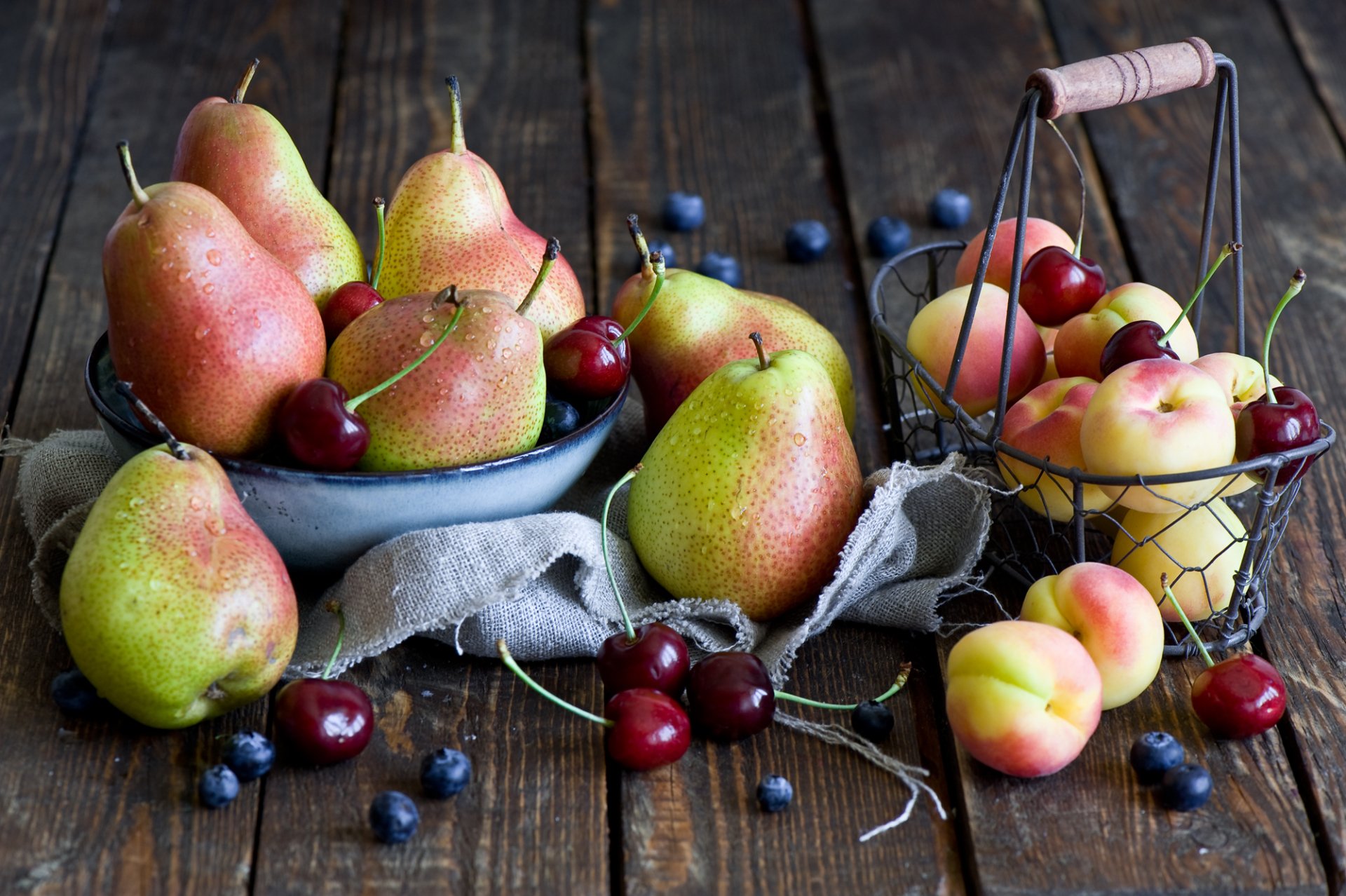 A still life HD desktop wallpaper featuring ripe pears, cherries, peaches, and scattered blueberries on a rustic wooden surface.