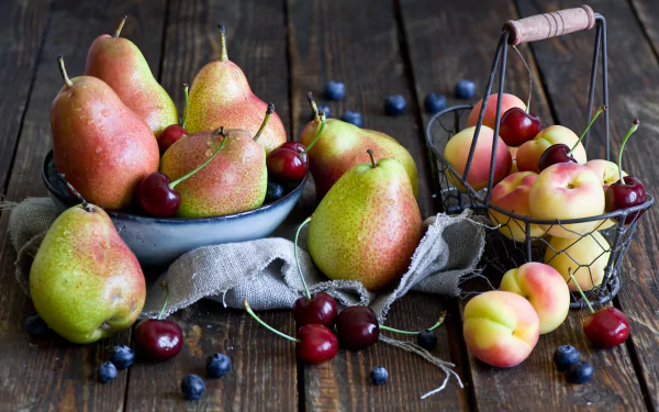 A still life HD desktop wallpaper featuring ripe pears, cherries, peaches, and scattered blueberries on a rustic wooden surface.