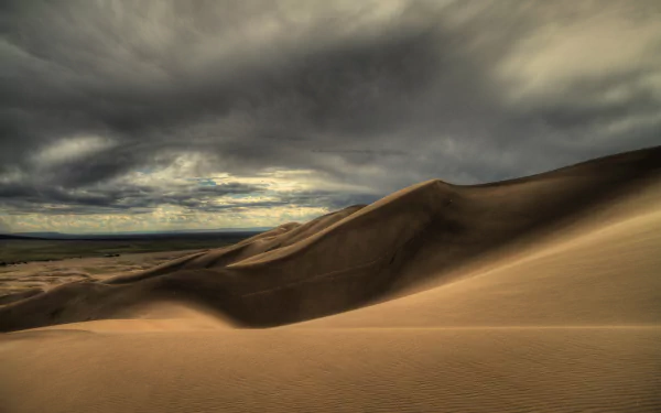 A 4K Ultra HD desert landscape wallpaper showcasing rolling sand dunes under a dramatic cloudy sky, capturing the raw beauty of nature in high detail.