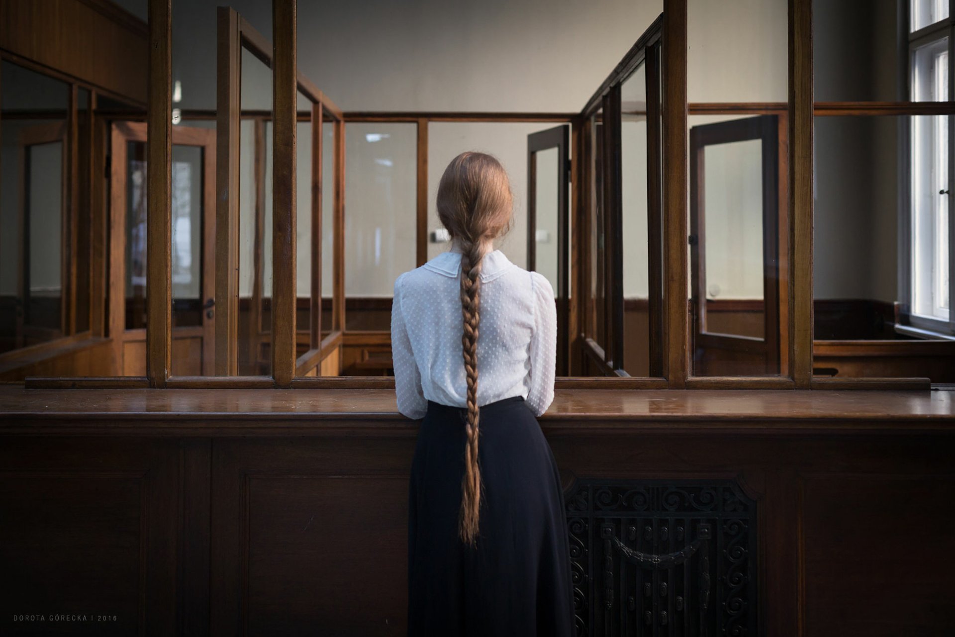 HD desktop wallpaper showing a brunette woman with a long braid viewed from the rear, standing in a room with multiple mirrors and framed windows.