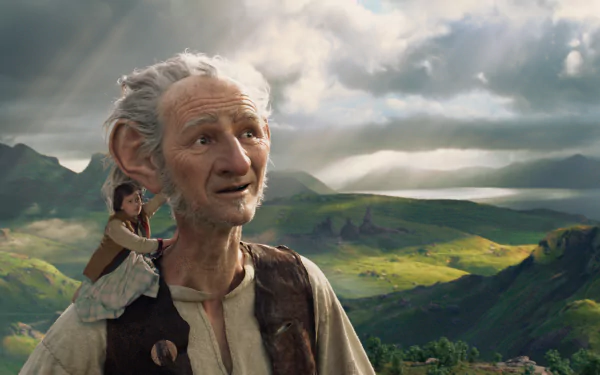 A scene from the movie The BFG (2016), featuring a giant with soft features and a small girl on his shoulder, set against a lush, mountainous landscape under a dramatic sky.