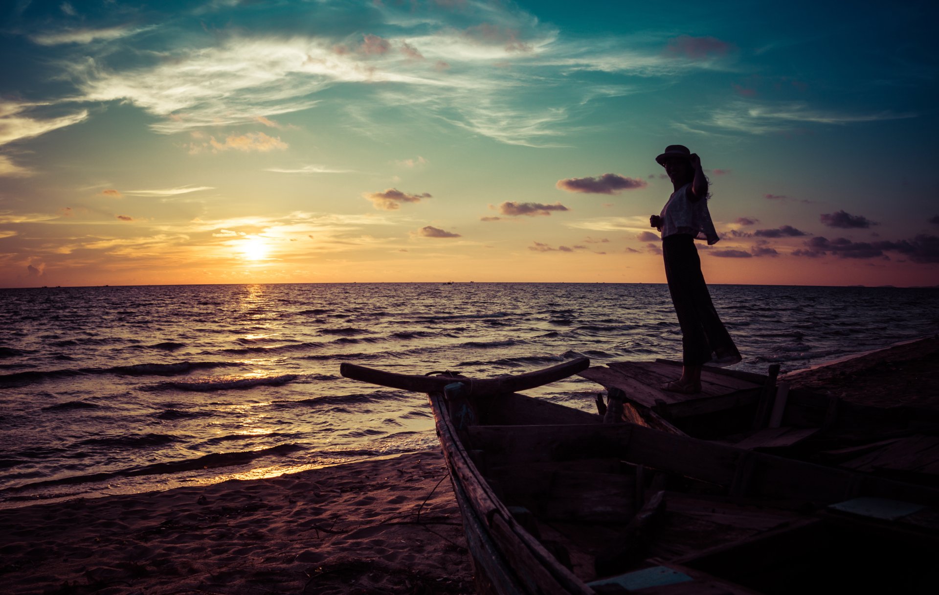 A woman wearing a hat stands on a boat by the sea, gazing at a vibrant summer sunset, captured in stunning 4K Ultra HD for a serene mood.