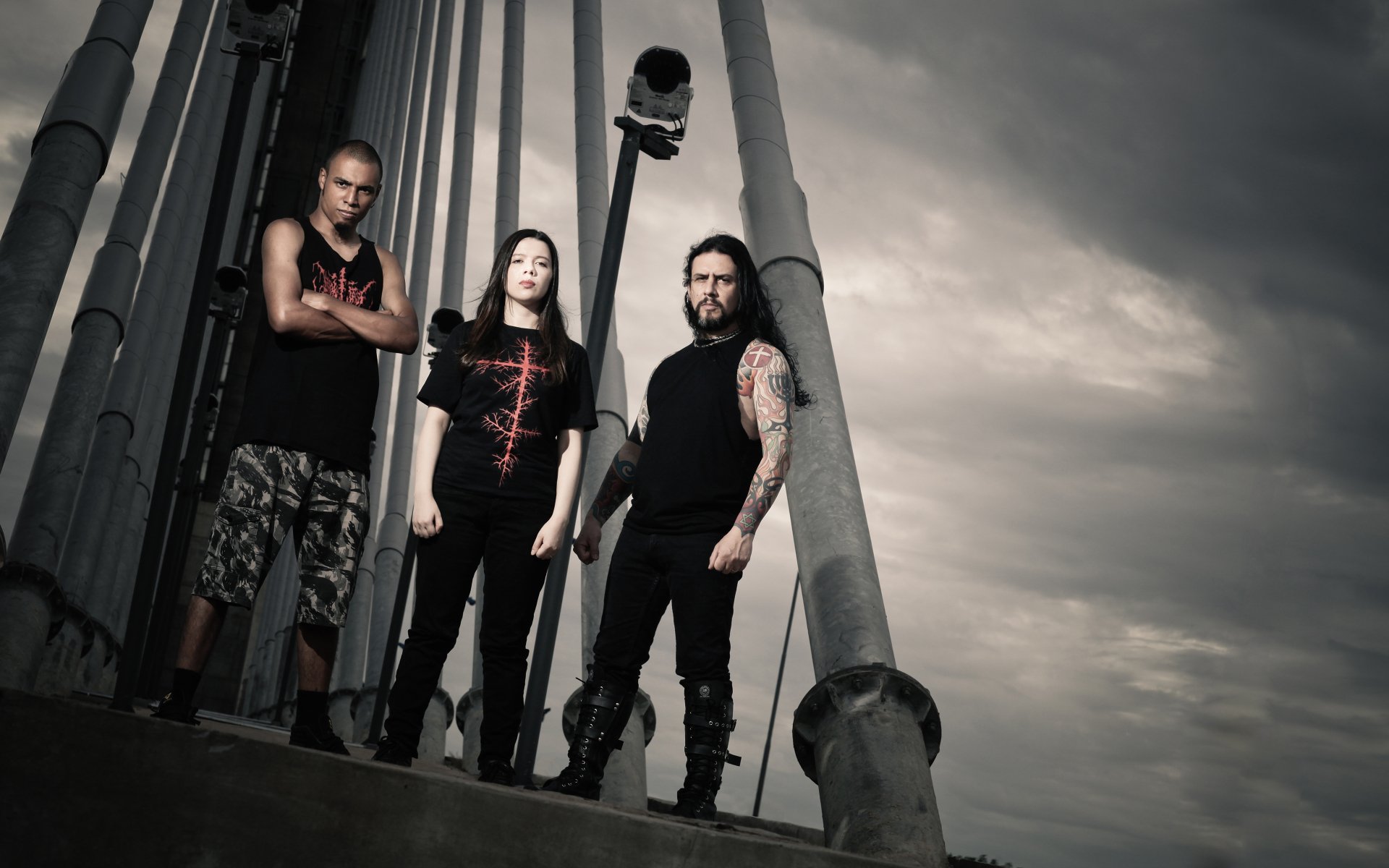 Moody 4K Ultra HD PC desktop wallpaper of Antidemon band — three musicians pose against industrial pillars under a stormy sky, dark music aesthetic.