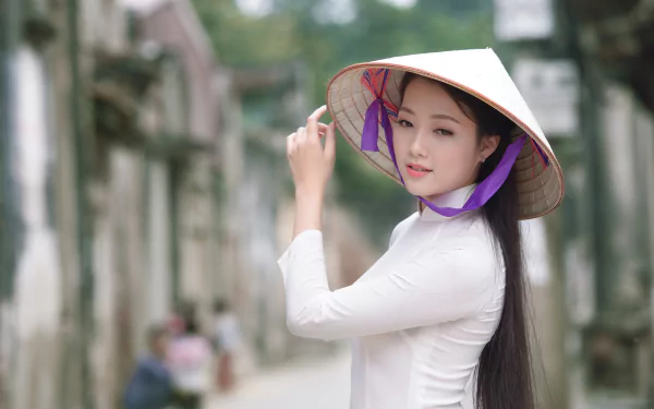 A woman in a Vietnamese ao dai and conical hat stands confidently, surrounded by a soft bokeh background, embodying the beauty of Vietnamese culture.