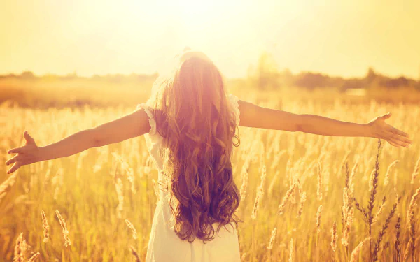 A woman stands in a sunlit field of tall grass, arms outstretched, basking in the warm glow of nature and sunshine, captured in vibrant 4K Ultra HD detail.
