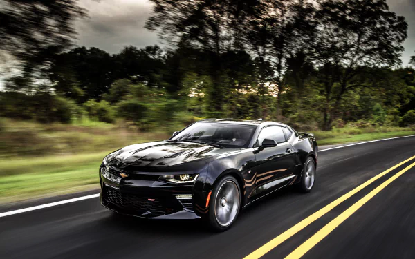 A black Chevrolet Camaro SS muscle car driving on a tree-lined road, captured in high-definition as a striking PC desktop wallpaper.