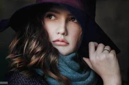 A close-up of a brunette woman with brown eyes, wearing a stylish scarf and a wide-brimmed hat, exuding elegance and poise against a soft backdrop.